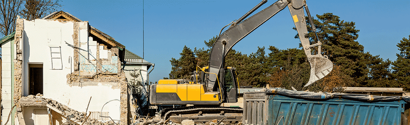 excavator on demolition site next to destroyed house and dumpster